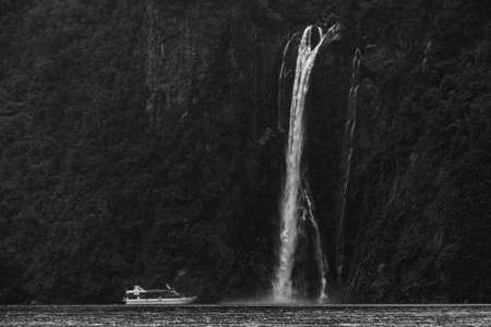 A stunning scene when a ferry cruising to a waterfall at Milford Sound, New Zealand. Black and white with high grain photo effect.