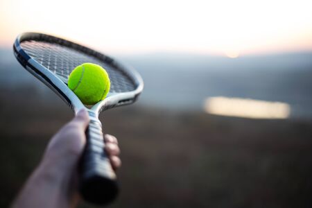 Close-up of male hand holding tennis racket with ball outdoors.